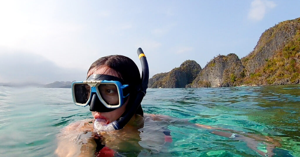 Girl snorkeling in blue waters with hills behind her